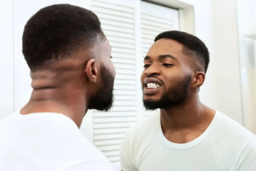 Homem negro olhando no espelho, verificando possível dor de dente.